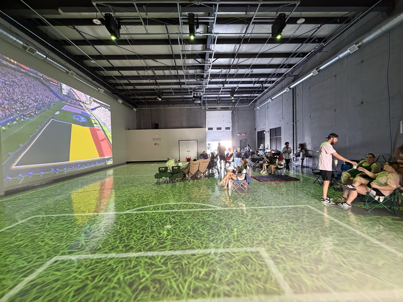 World Cup watch party with the match on the two-story wall and a grass pitch projected across the floor